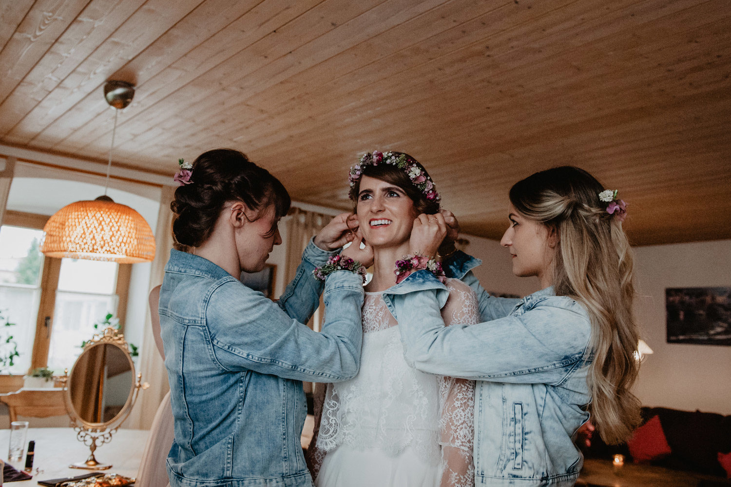 bride with flower crown getting ready on rustic farm with bridesmaids in denim jackets