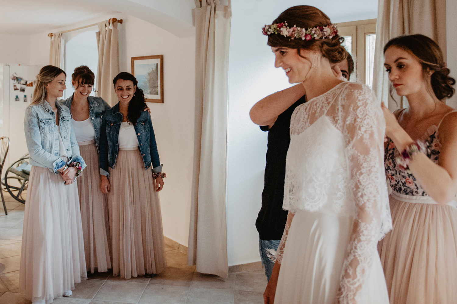 bridesmaids in pastel dresses and denim jackets watching bohemian bride with flower crown getting ready