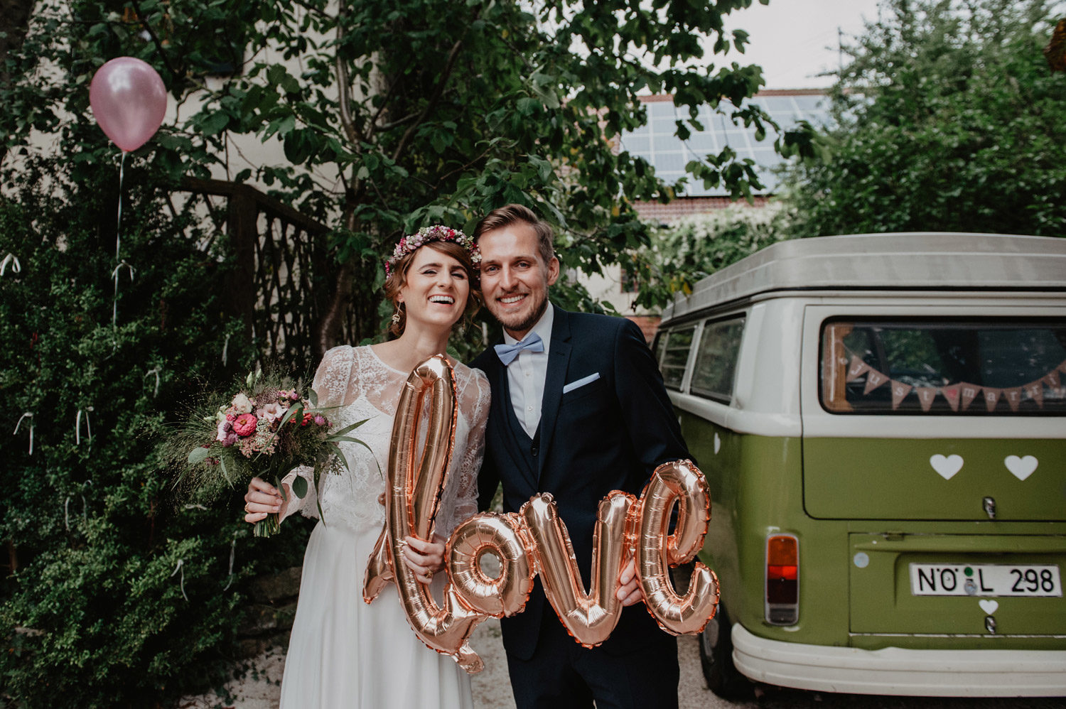 boho bride and groom in leafy garden holding love ballons