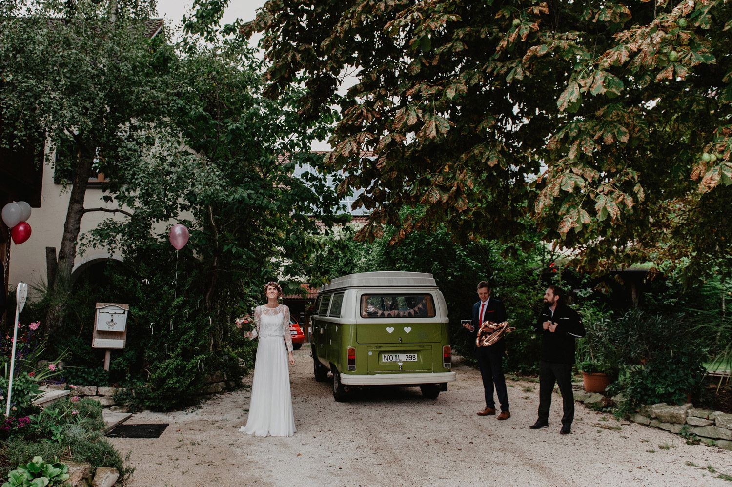 bride in modern elfenkleid wedding dress with lace top and flower crown laughing in front of VW wedding car