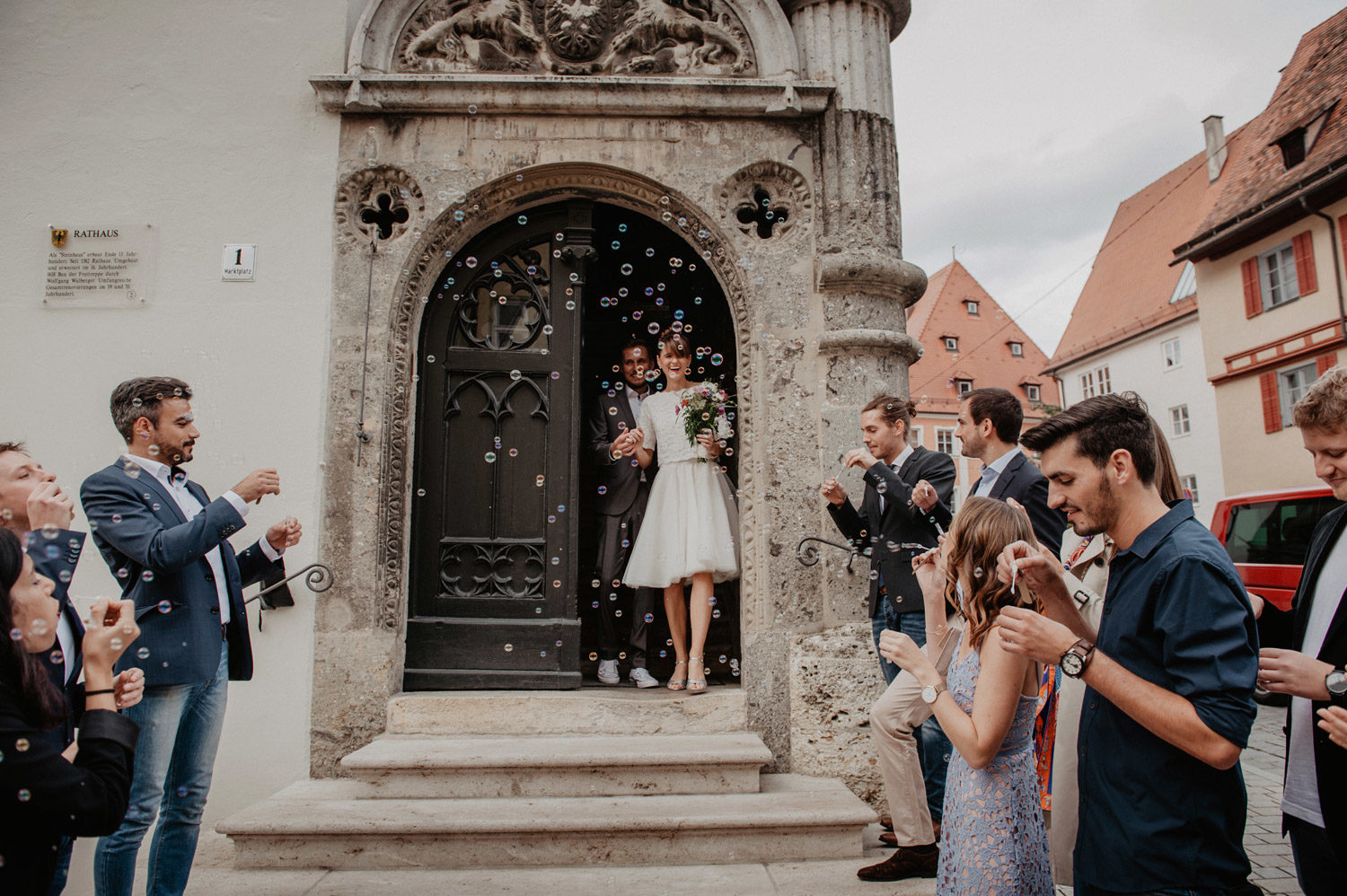 laughing bride and groom leaving medieval church with friends blowing bubbles