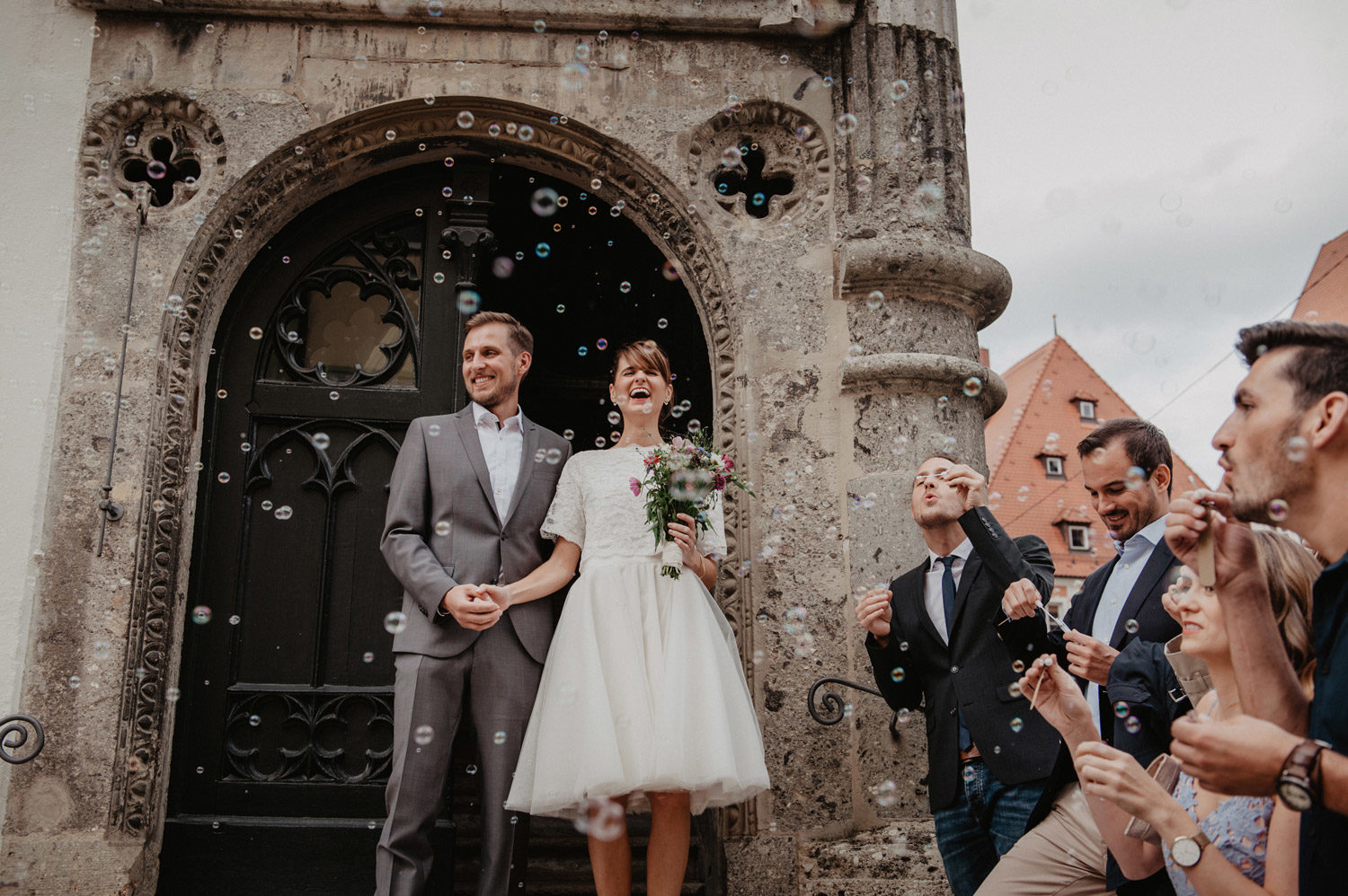 laughing young couple leaving medieval church showered in soap bubbles