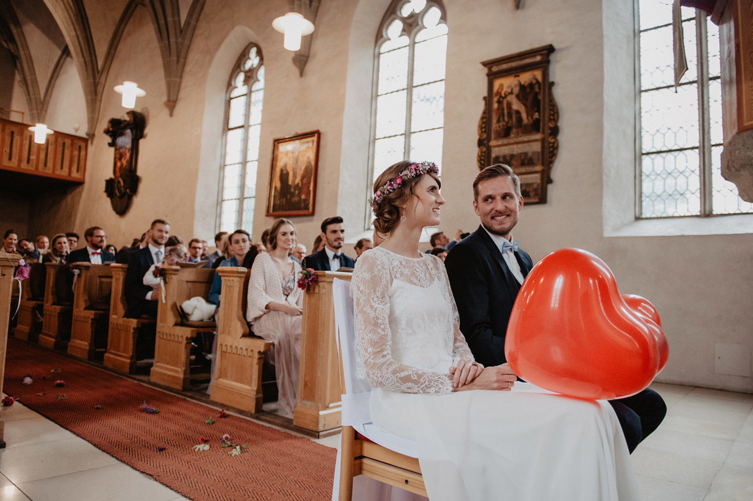 couple blowing up red heart balloons during boho church ceremony 