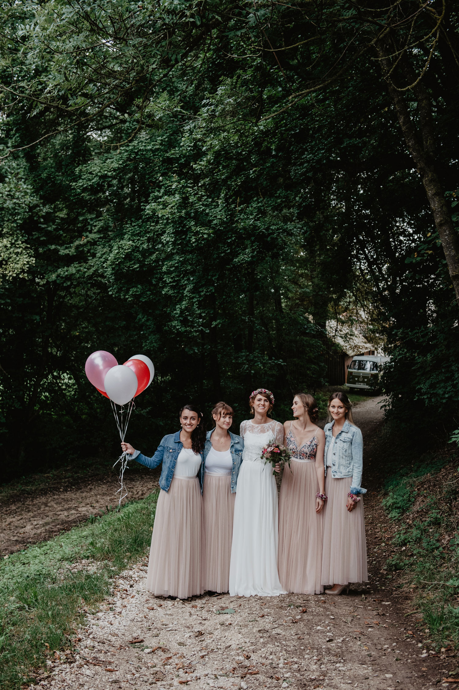 boho bride with flowercrown and bridesmaids in denim jackets pastel tulle skirts with balloons posing at tipi wedding in forest