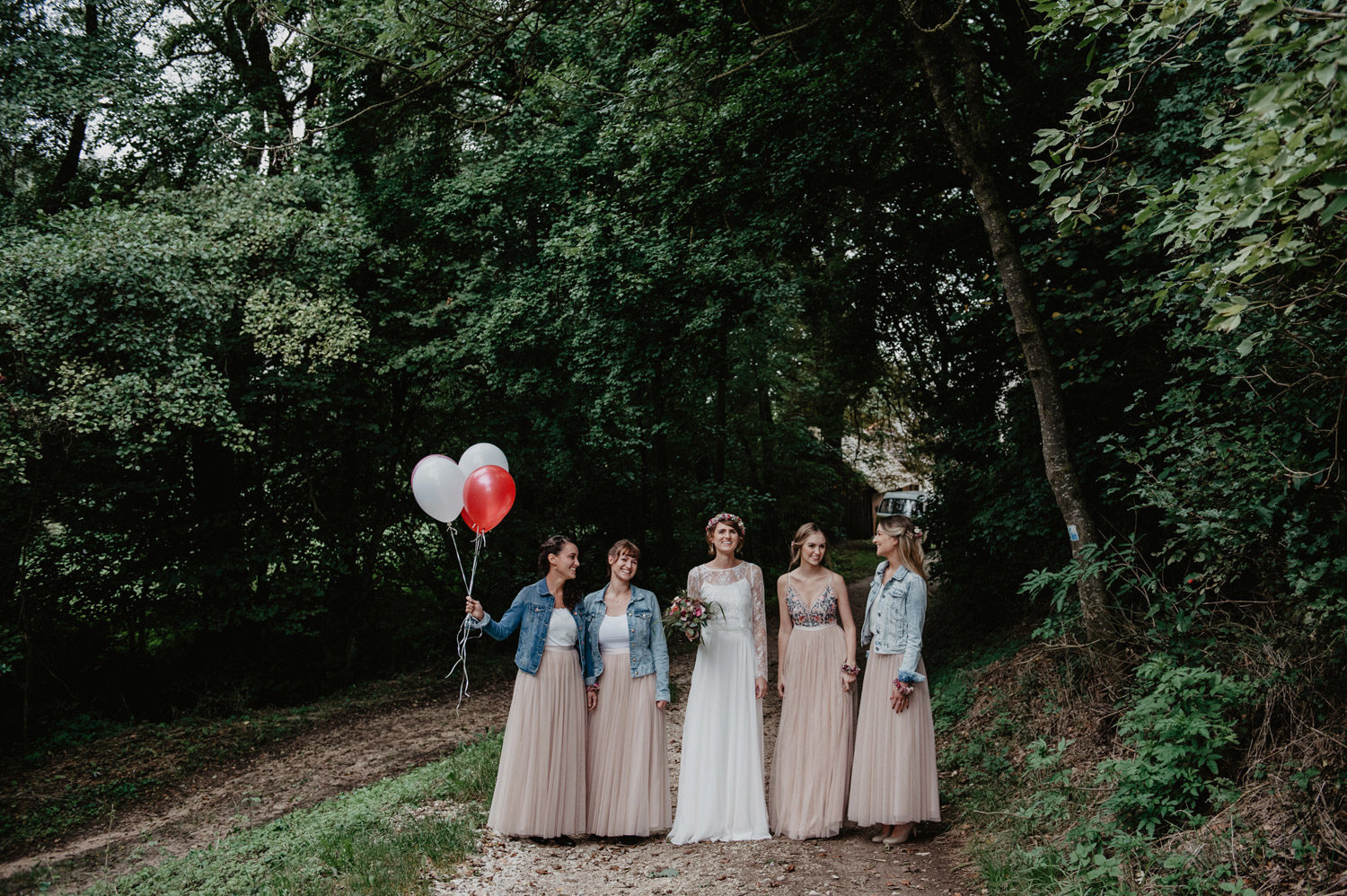 boho bride with flowercrown and bridesmaids in denim jackets pastel tulle skirts with balloons posing at tipi wedding in forest