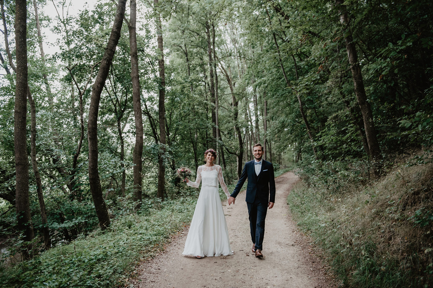 boho bride in elfenkleid wedding dress and groom walking in forest