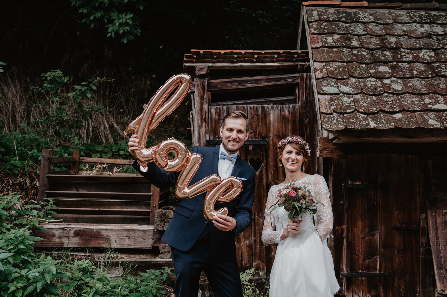 boho groom and bride holding love balloon sign in front of rustic barn